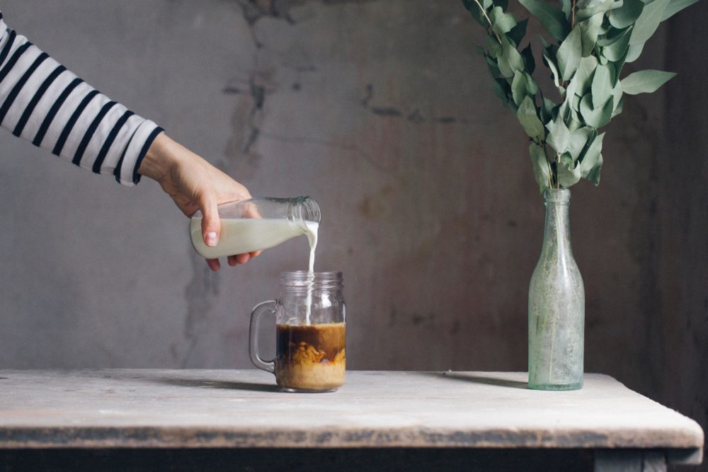 Hand pouring milk into a glass of coffee.